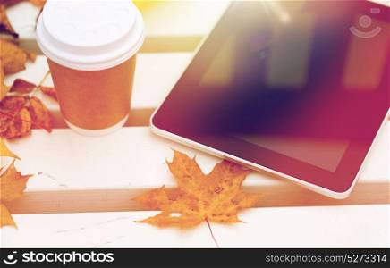 season, technology and advertisement concept - close up of tablet pc computer and coffee paper cup on bench in autumn park. tablet pc and coffee cup on bench in autumn park