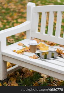 season, technology and advertisement concept - tablet pc computer and coffee paper cup on bench in autumn park