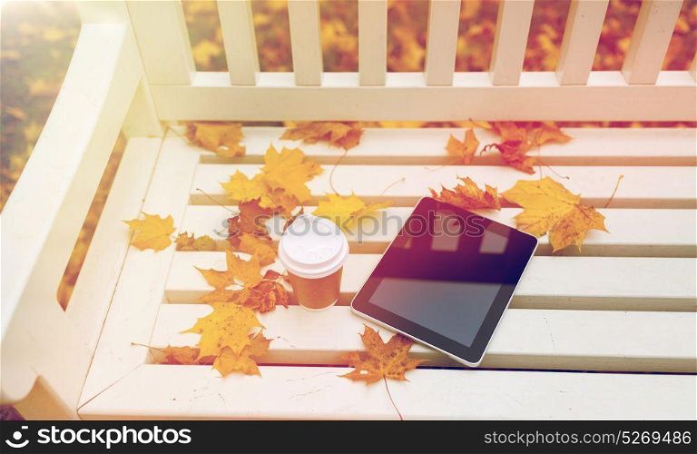 season, technology and advertisement concept - tablet pc computer and coffee paper cup on bench in autumn park. tablet pc and coffee cup on bench in autumn park