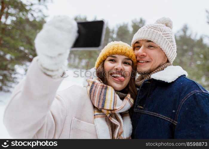 season, technology and leisure concept - happy couple with smartphone taking selfie in winter park. couple with smartphone taking selfie in winter