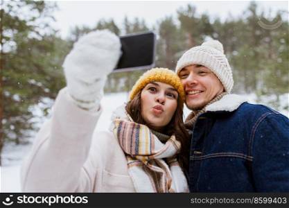 season, technology and leisure concept - happy couple with smartphone taking selfie in winter park. couple with smartphone taking selfie in winter