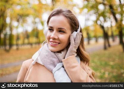 season, technology and people concept - beautiful happy young woman with headphones listening to music in autumn park