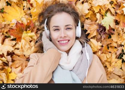 season, technology and people concept - beautiful happy young woman with headphones lying on autumn leaves listening to music