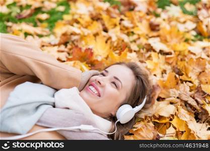 season, technology and people concept - beautiful happy young woman with headphones lying on autumn leaves listening to music