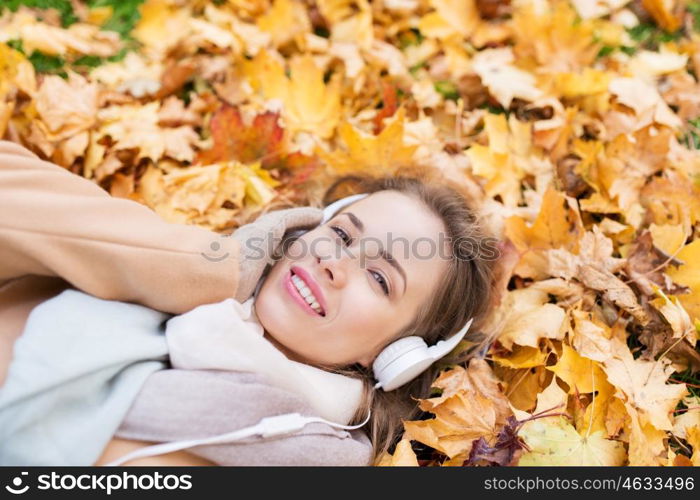 season, technology and people concept - beautiful happy young woman with headphones lying on autumn leaves listening to music