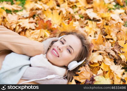 season, technology and people concept - beautiful happy young woman with headphones lying on autumn leaves listening to music