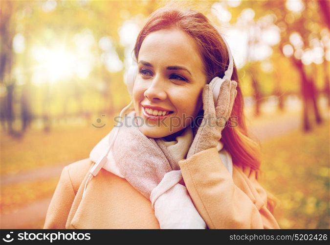 season, technology and people concept - beautiful happy young woman with headphones listening to music in autumn park. woman in headphones listening music at autumn park