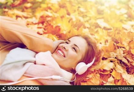 season, technology and people concept - beautiful happy young woman with headphones lying on autumn leaves listening to music. woman with headphones listening to music in autumn