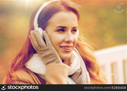 season, technology and people concept - beautiful happy young woman with headphones listening to music and sitting on bench in autumn park. happy woman with headphones in autumn park