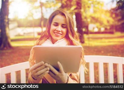 season, technology and people concept - beautiful happy young woman with tablet pc computer sitting on bench in autumn park. happy young woman with tablet pc in autumn park