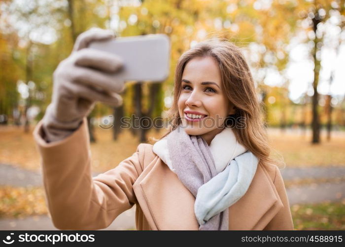 season, technology and people concept - beautiful young happy woman taking selfie with smartphone in autumn park