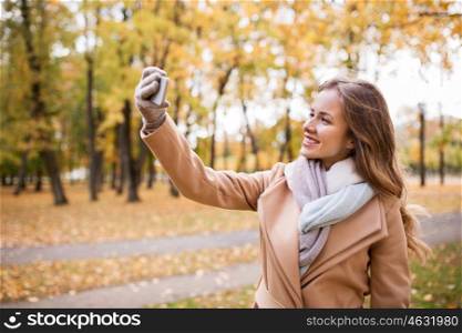 season, technology and people concept - beautiful young happy woman taking selfie with smartphone in autumn park