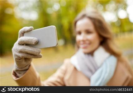 season, technology and people concept - beautiful young happy woman taking selfie with smartphone in autumn park