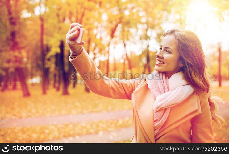 season, technology and people concept - beautiful young happy woman taking selfie with smartphone in autumn park. woman taking selfie by smartphone in autumn park