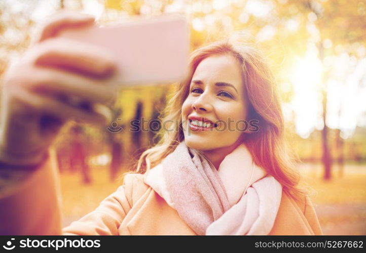 season, technology and people concept - beautiful young happy woman taking selfie with smartphone in autumn park. woman taking selfie by smartphone in autumn park