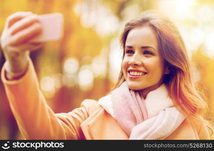 season, technology and people concept - beautiful young happy woman taking selfie with smartphone in autumn park. woman taking selfie by smartphone in autumn park