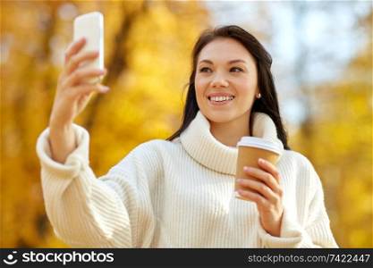 season, technology and people concept - beautiful young happy woman taking selfie by smartphone at autumn park. woman taking selfie by smartphone at autumn park