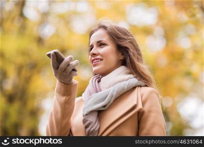 season, technology and people concept - beautiful young woman in autumn park and using voice command recorder on smartphone