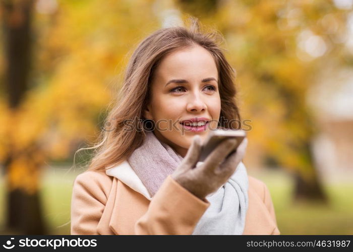 season, technology and people concept - beautiful young woman walking in autumn park and using voice command recorder on smartphone