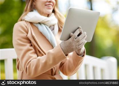season, technology and people concept - close up of beautiful happy young woman with tablet pc computer sitting on bench in autumn park
