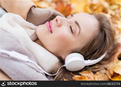 season, technology and people concept - close up of beautiful happy young woman with headphones lying on autumn leaves listening to music