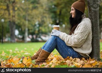 season, technology and people concept - close up of happy young woman drinking coffee from paper cup in autumn park