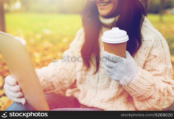 season, technology and people concept - close up of young smiling woman with tablet pc and coffee cup in autumn park. woman with tablet pc and coffee cup in autumn park