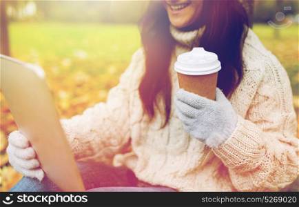 season, technology and people concept - close up of young smiling woman with tablet pc and coffee cup in autumn park. woman with tablet pc and coffee cup in autumn park