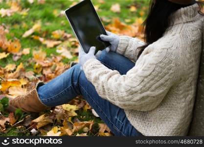 season, technology and people concept - close up of young woman with tablet pc computer sitting on grass in autumn park