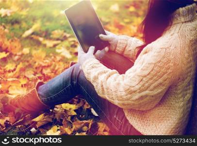 season, technology and people concept - close up of young woman with tablet pc computer sitting on grass in autumn park. close up of woman with tablet pc in autumn park