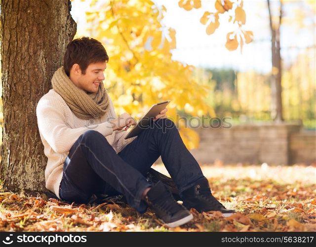 season, technology and people concept - smiling young man with tablet pc computer in autumn park