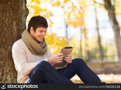 season, technology and people concept - smiling young man with tablet pc computer in autumn park
