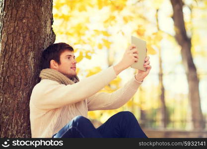 season, technology and people concept - smiling young man with tablet pc computer in autumn park