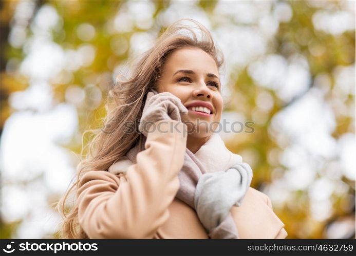 season, technology, communication and people concept - beautiful young woman in autumn park calling on smartphone
