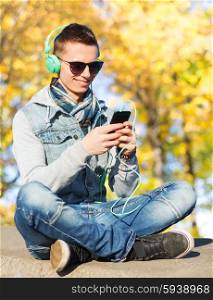 season, technology, lifestyle and people concept - smiling young man or teenage boy in headphones with smartphone listening to music over autumn park background