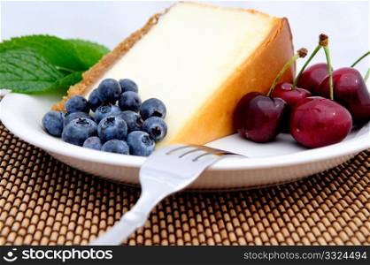 Seasonal fruit with a slice of plain cheese cake with a mint leaf garnish served on a white saucer. Blueberries and Bing cherries . Cheese Cake, Cherries And Blueberries