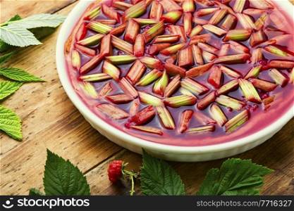 Seasonal pie or cake with rhubarb stalks and raspberries. Summer sweet dessert.. Pie with rhubarb and raspberries on old wooden background