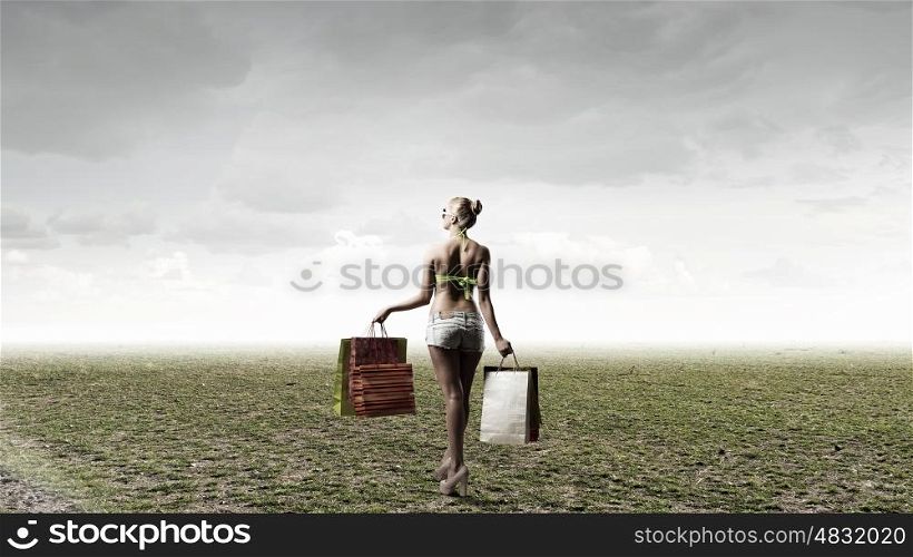 Seasonal sale. Rear view of young pretty woman in bikini and shorts with shopping bags