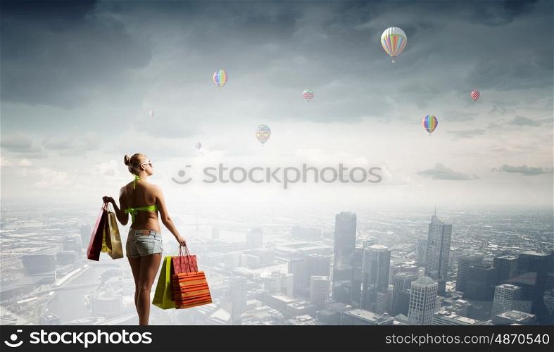 Seasonal sale. Rear view of young pretty woman in bikini and shorts with shopping bags