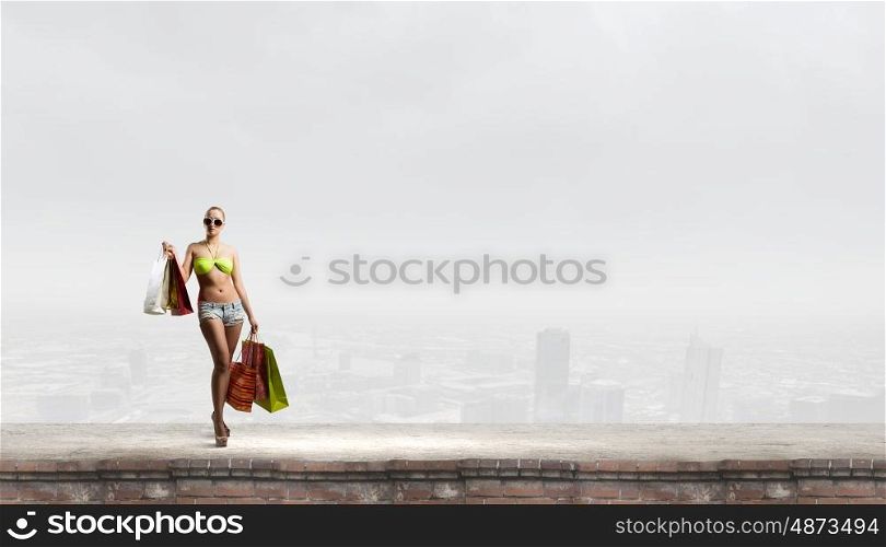 Seasonal sale. Young pretty woman in bikini and shorts with shopping bags