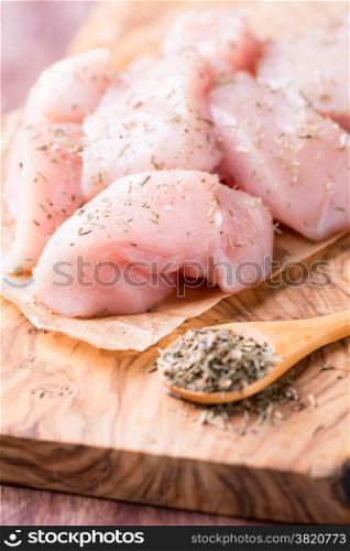 Seasoned raw chicken breast fillets over wooden board, selective focus