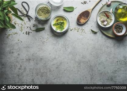 Seasoning background with flavor herbs, spices. herbal salt,  olive oil and wooden spoon for tasty cooking. Top view. Border with copy space