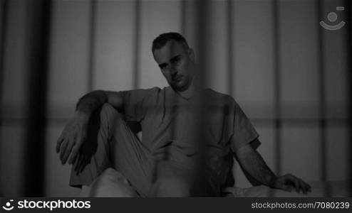Seated inmate in prison stares at camera (B/W Version)