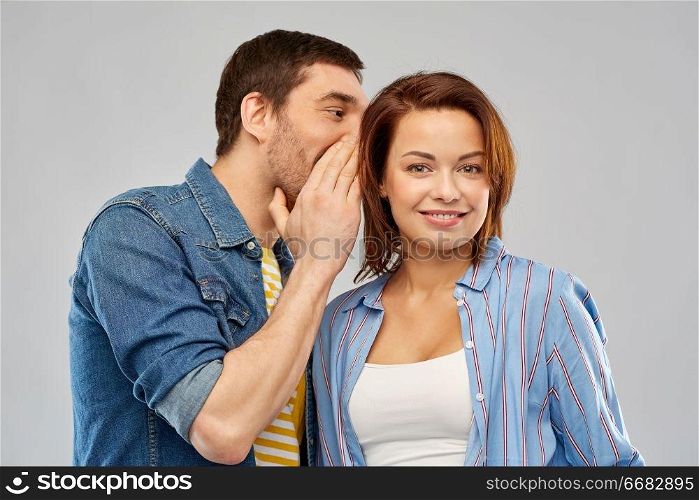 secret and people concept - happy couple whispering over grey background. happy couple whispering over grey background