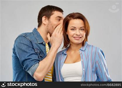 secret and people concept - happy couple whispering over grey background. happy couple whispering over grey background