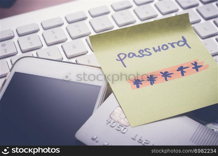 Secret password written on yellow paper note stick on keyboard with mobile phone and credit card on background, vintage dark tone. Internet banking, payment, data privacy, online security concepts.