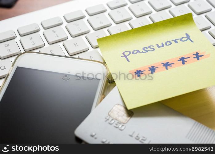 Secret password written on yellow paper note stick on white keyboard with blank screen of smartphone and credit card on background. Internet banking, purchase, data privacy, cyber security concepts.