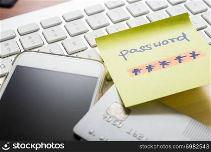 Secret password written on yellow paper note stick on white keyboard with blank screen of smartphone and credit card on background. Internet banking, purchase, data privacy, cyber security concepts.