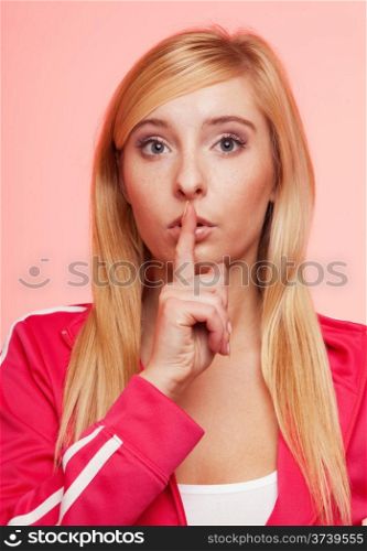 Secret woman. Sporty fit fitnrss blonde girl showing hand silence sign, saying hush be quiet on pink background
