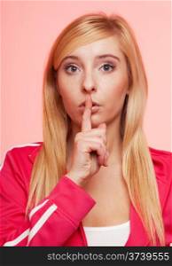 Secret woman. Sporty fit fitnrss blonde girl showing hand silence sign, saying hush be quiet on pink background